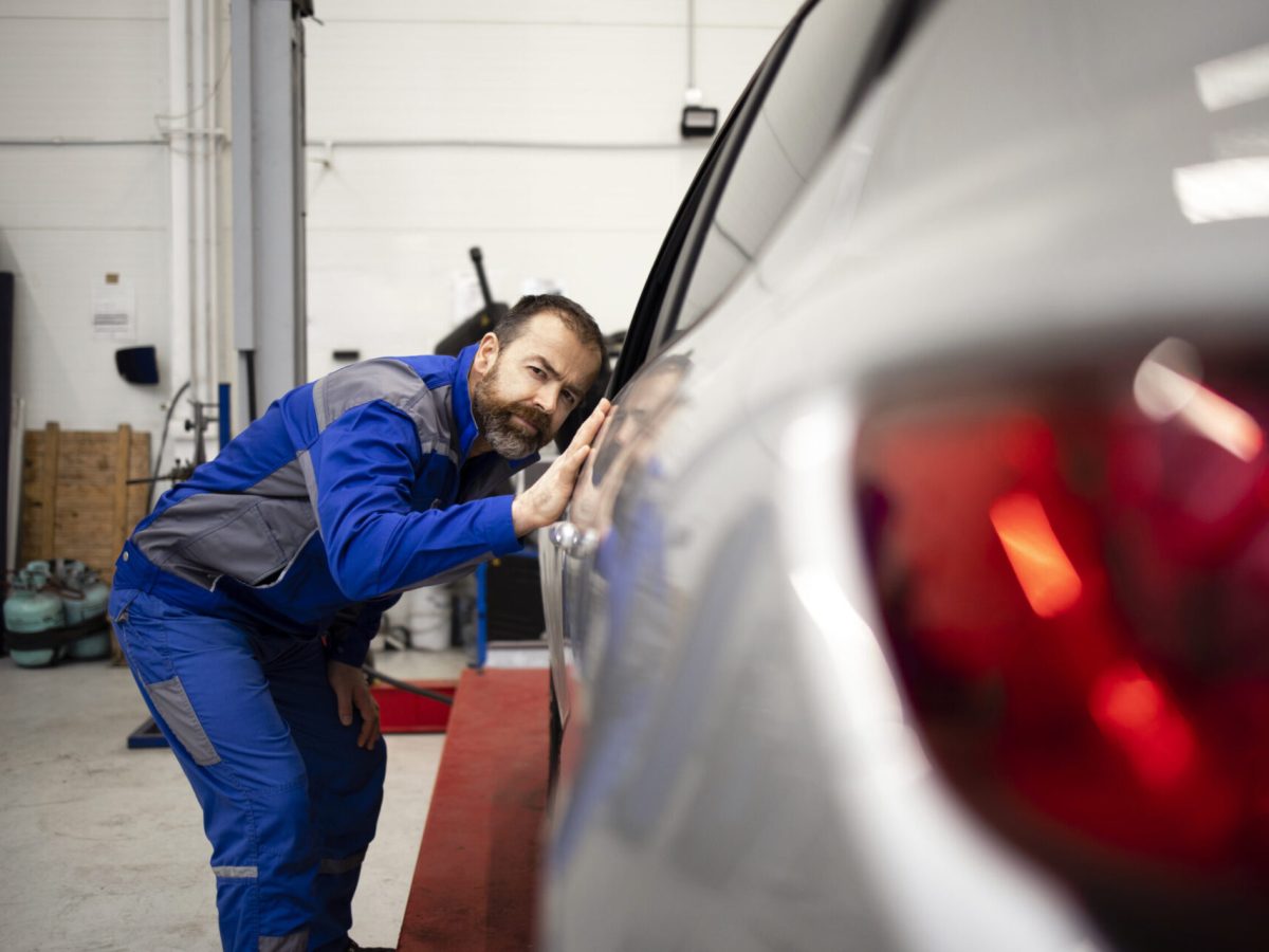 Professional car mechanic checking vehicle body in workshop. Automobile service and maintenance.